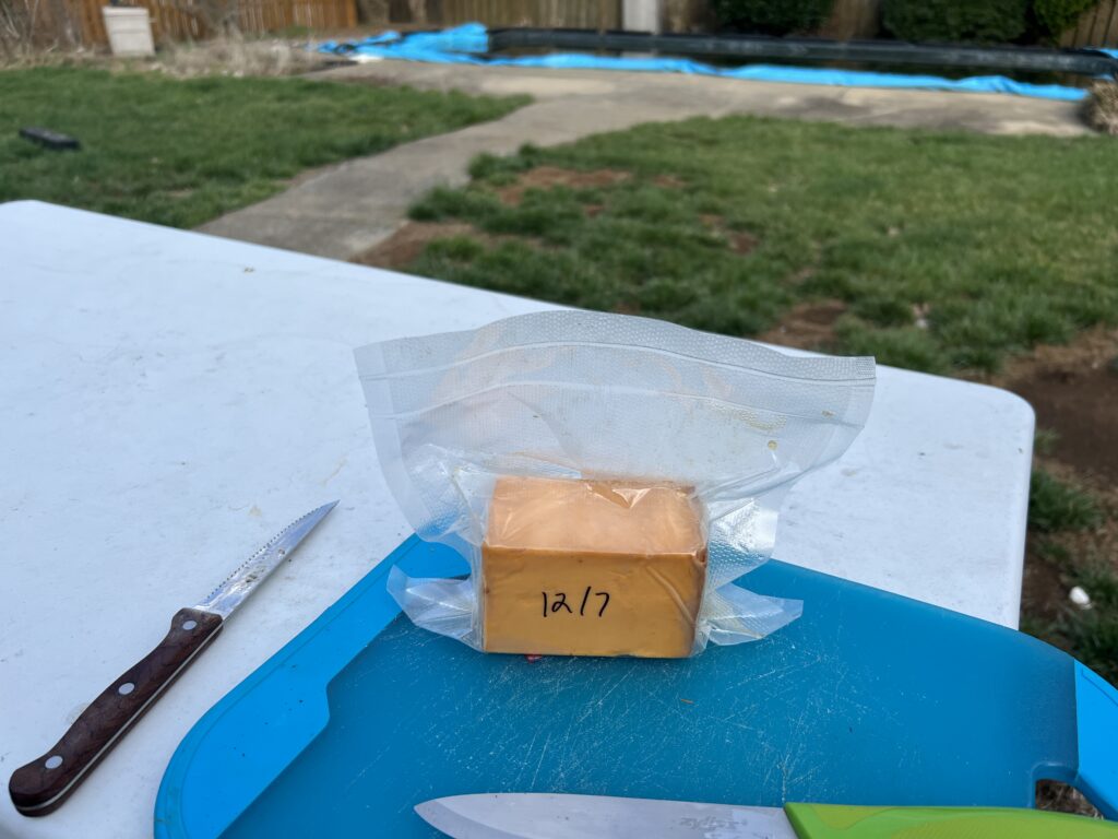 A block of homemade smoked cheese, dated 12/7, on a cutting board ready to top the burgers