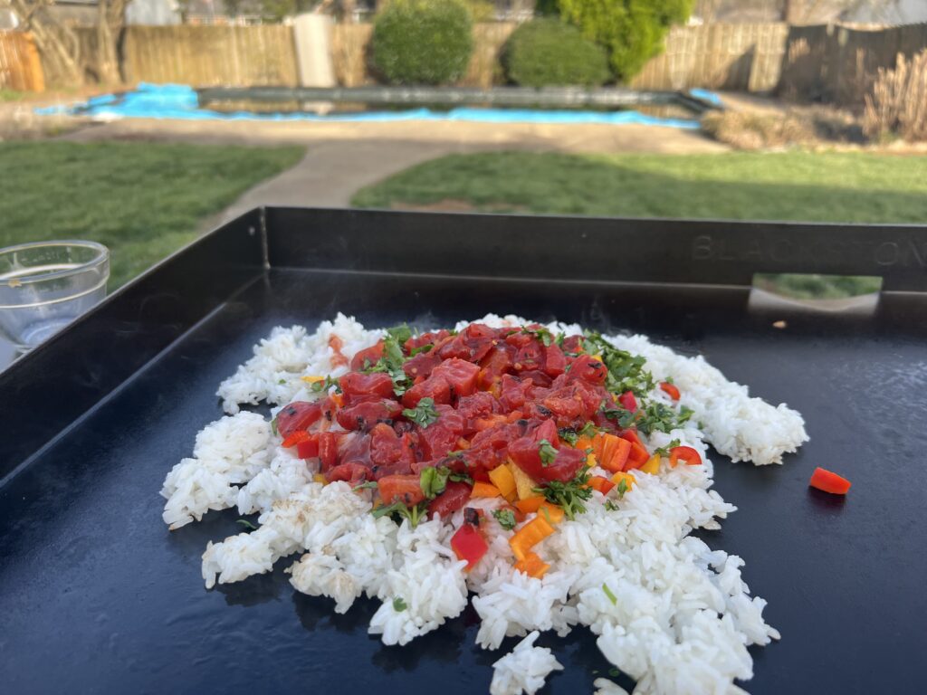 Rice topped with diced peppers and herbs on the griddle, before adding the beef