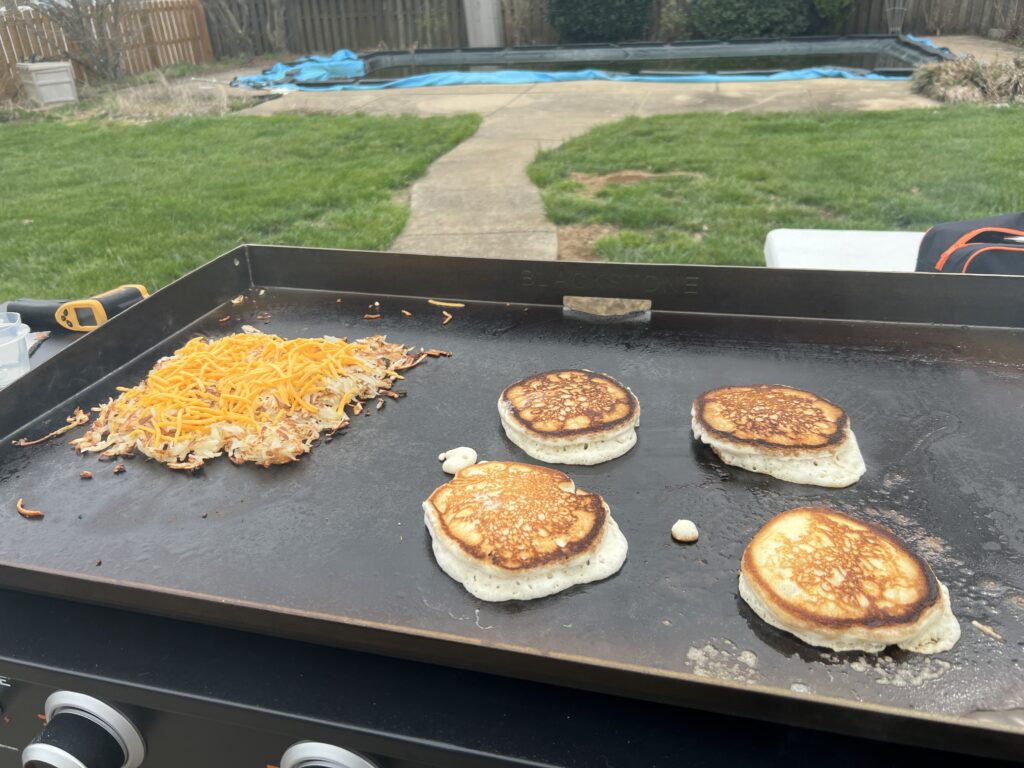Pancakes and cheesy hash browns cooking, pancakes browning unevenly from too-high heat
