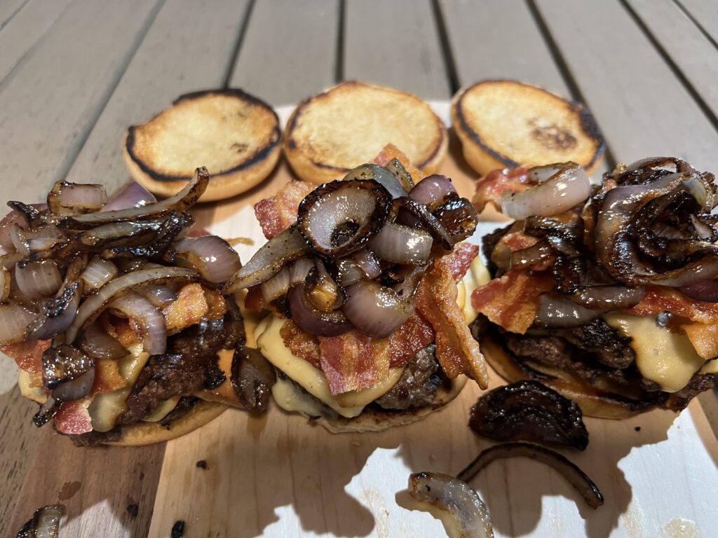Finished beef smash burgers topped with melted white cheddar, bacon, and grilled onions