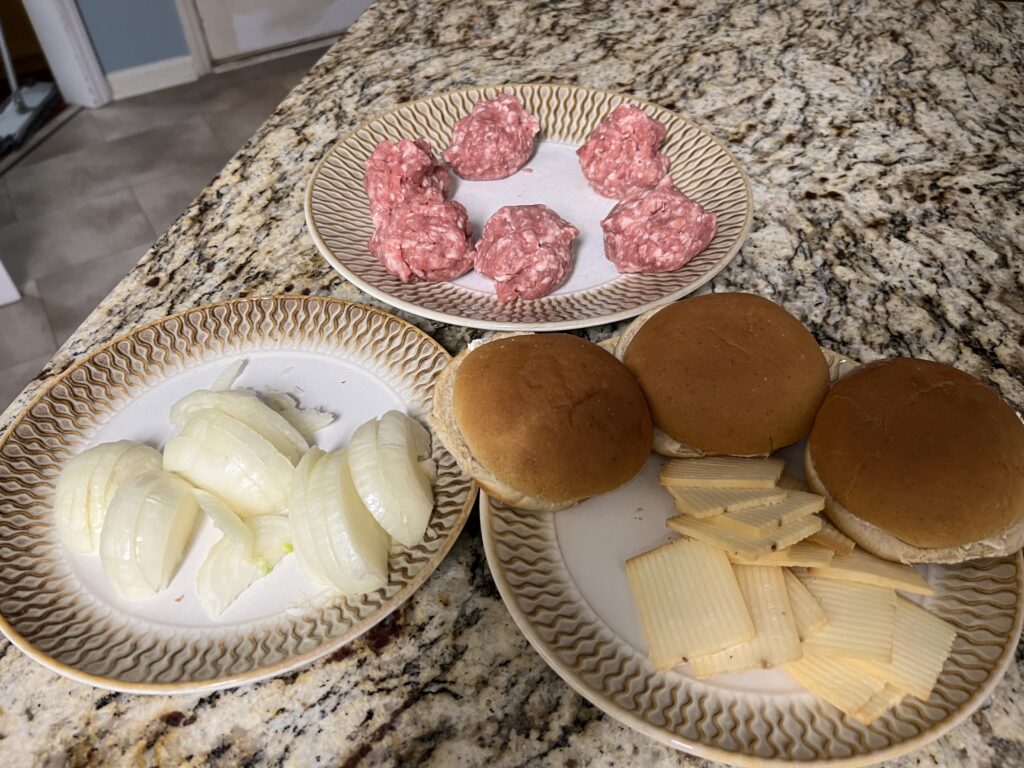 Ground pork portioned into balls, sliced onions, and sliced white cheddar cheese prepped on the counter