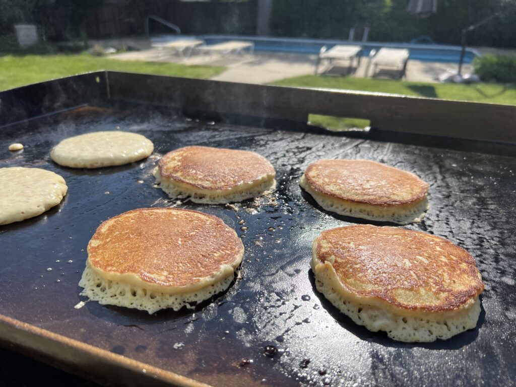 Pancakes cooking on the griddle, some just poured and some flipped
