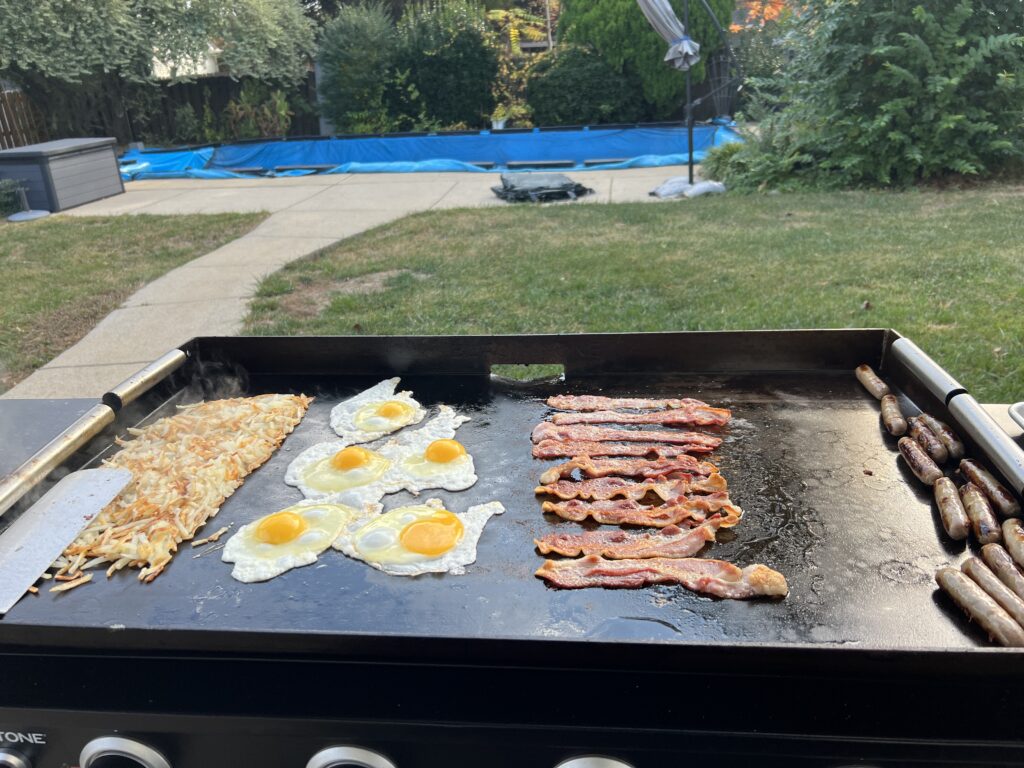 Hash browns, eggs, bacon, and sausage cooking together on the Blackstone