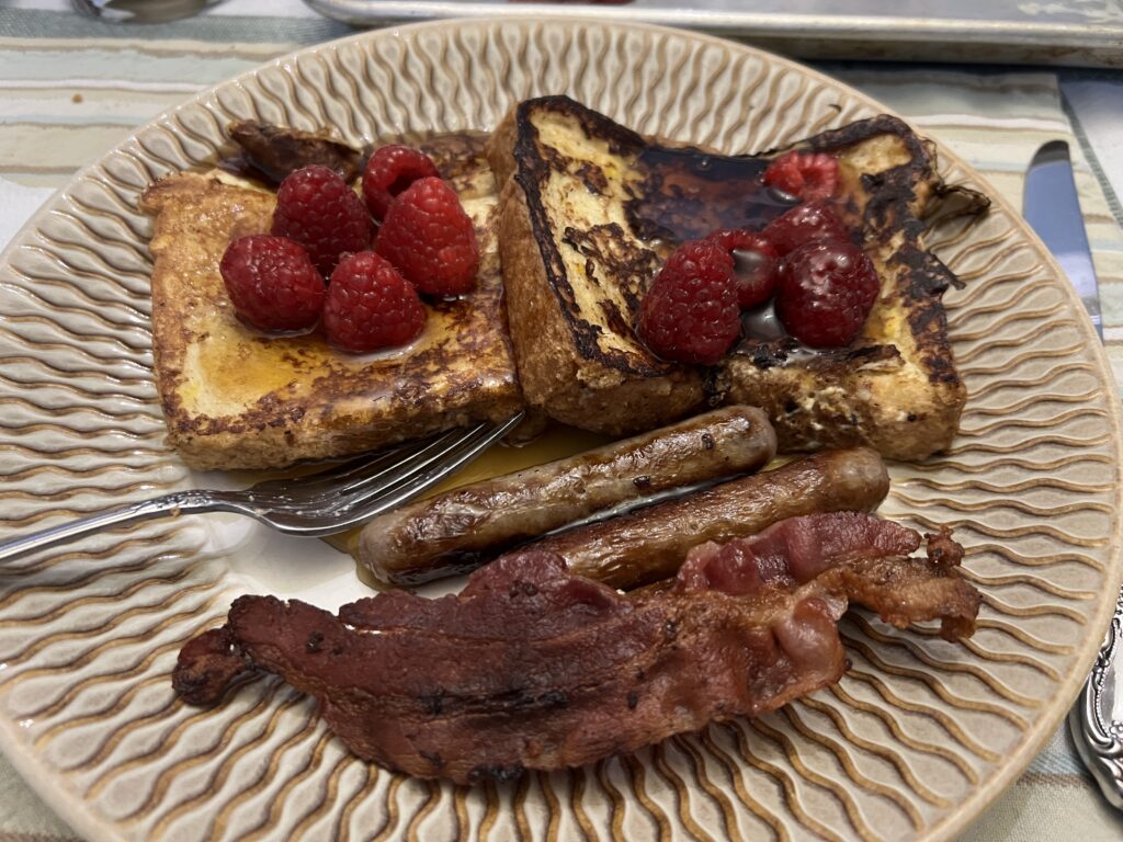 A second plate of french toast, topped with raspberries and served with bacon and sausage