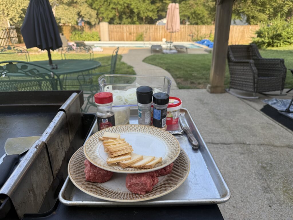 Ground beef, sliced cheese, and seasonings staged for onion smash burgers on a Blackstone griddle