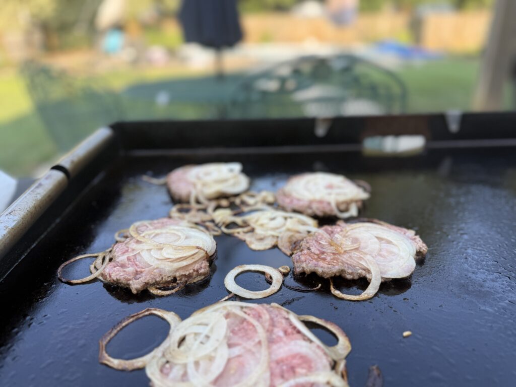 Onion smash burger patties with caramelized onions cooking undisturbed on the Blackstone griddle