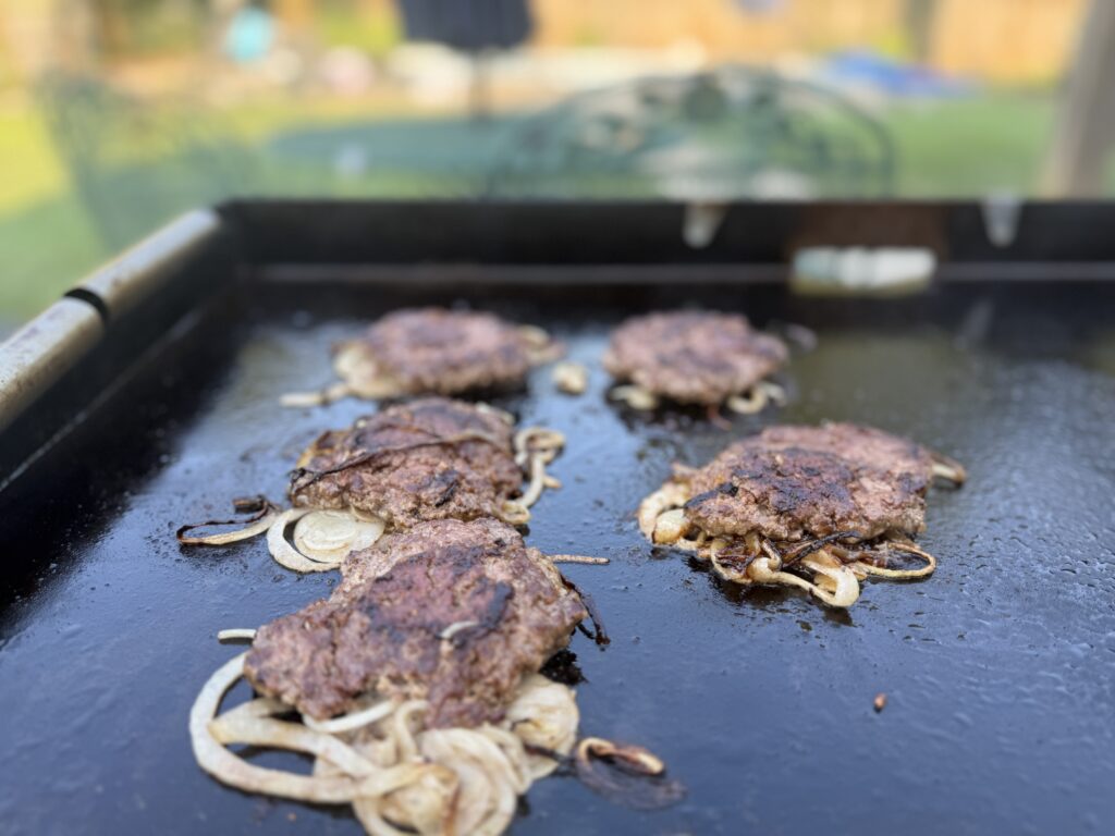 Deeply caramelized onions under the smash burger patties on a Blackstone griddle,after the flip