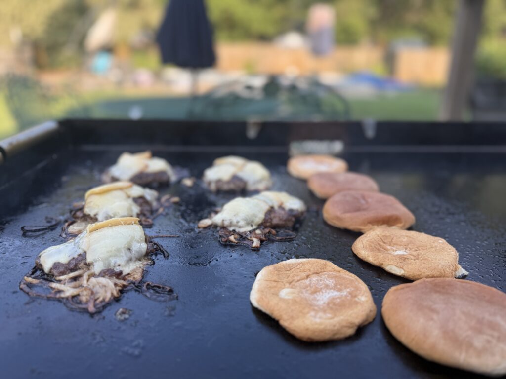  Finished onion smash burgers with melted smoked cheddar next to toasted buns on a sheet pan from the Blackstone griddle
